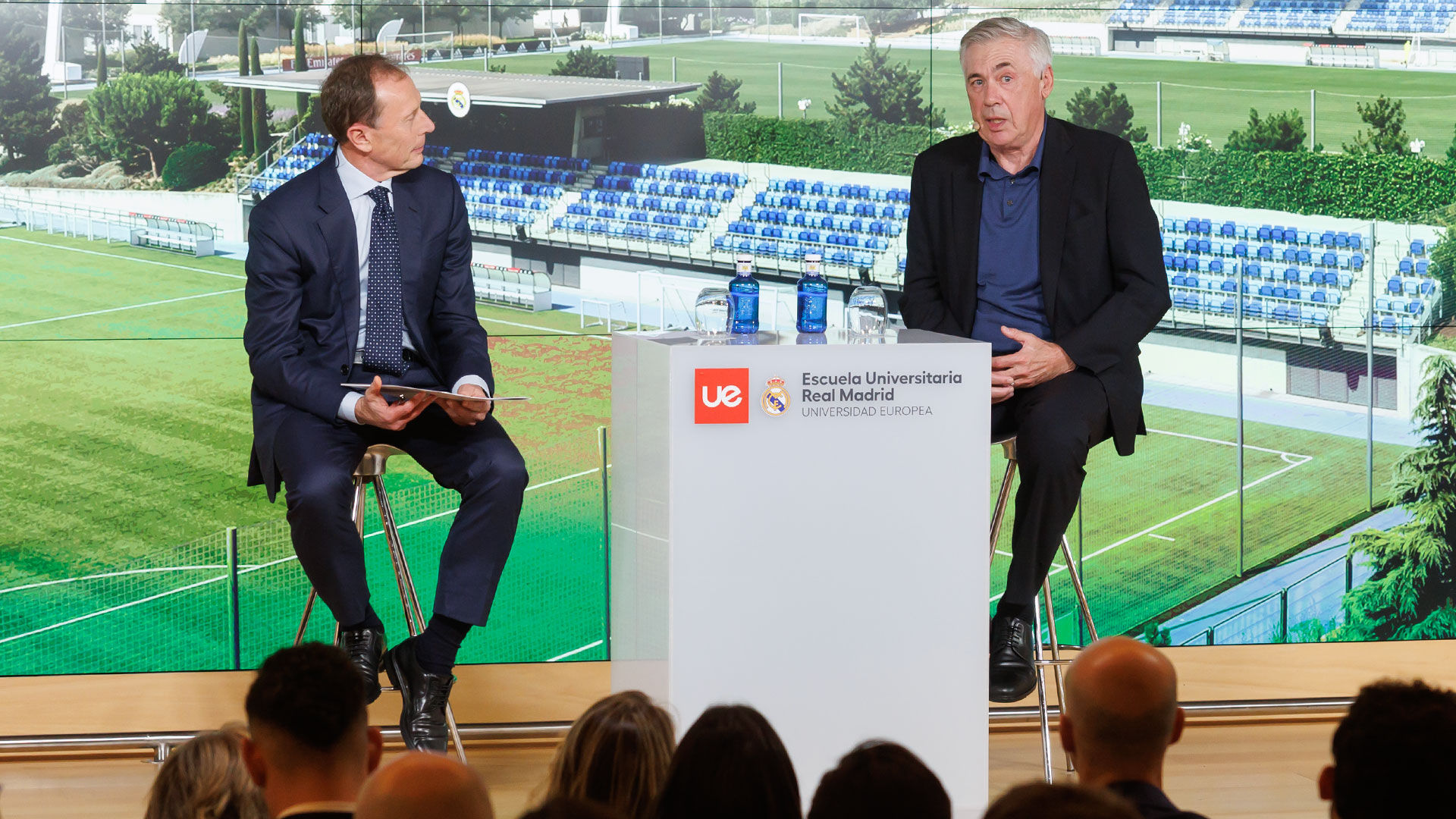 Carlo Ancelotti sentado, junto a Emilio Butragueño, durante una charla con la Escuela Universitaria Real Madrid Universidad Europea.