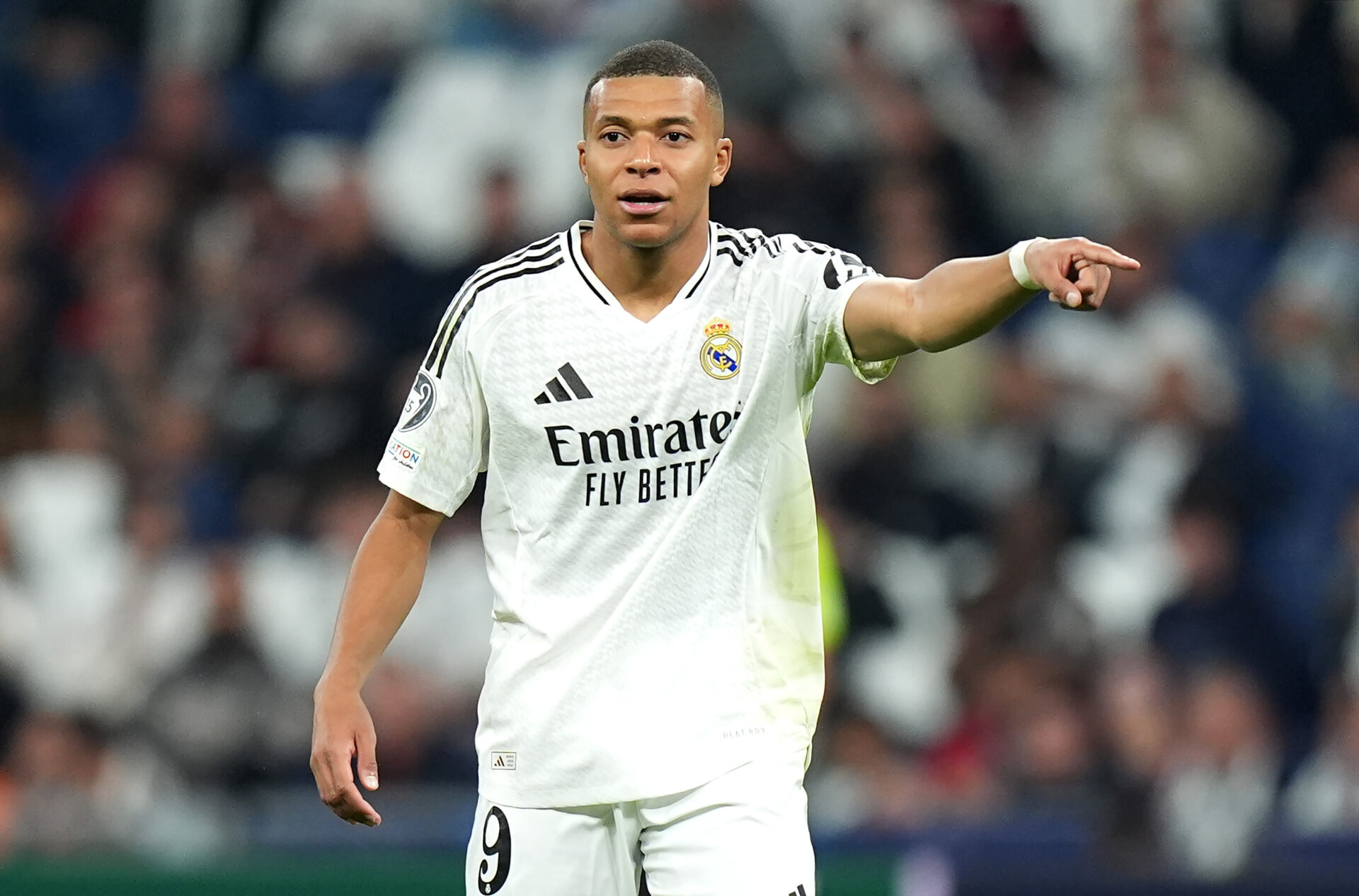 Kylian Mbappé, con la camiseta del Real Madrid, señala con su brazo izquierdo.