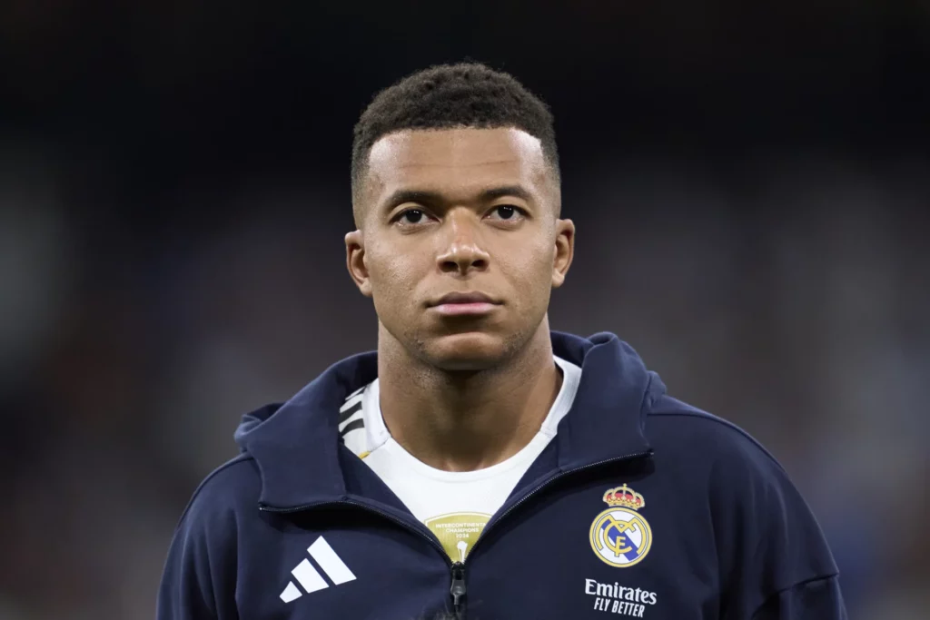 Mbappé, concentrado con una chaqueta de chándal azul oscuro, antes de un partido del Real Madrid.