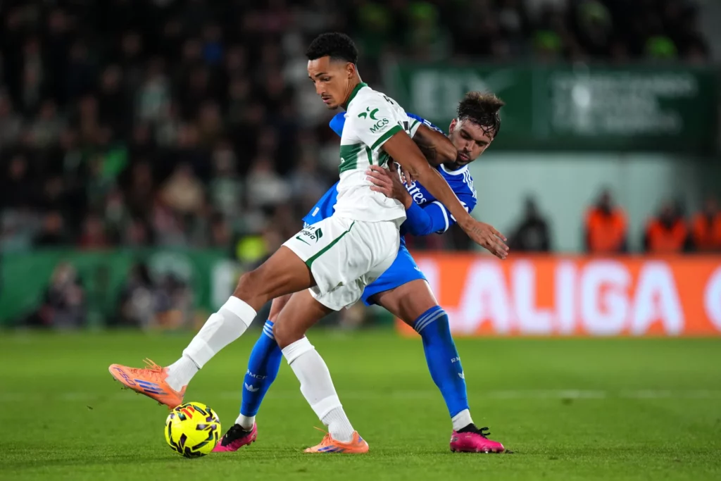 Raúl Asencio pugna con Álvaro Rodríguez por la pelota durante el Elche CF - Real Madrid.
