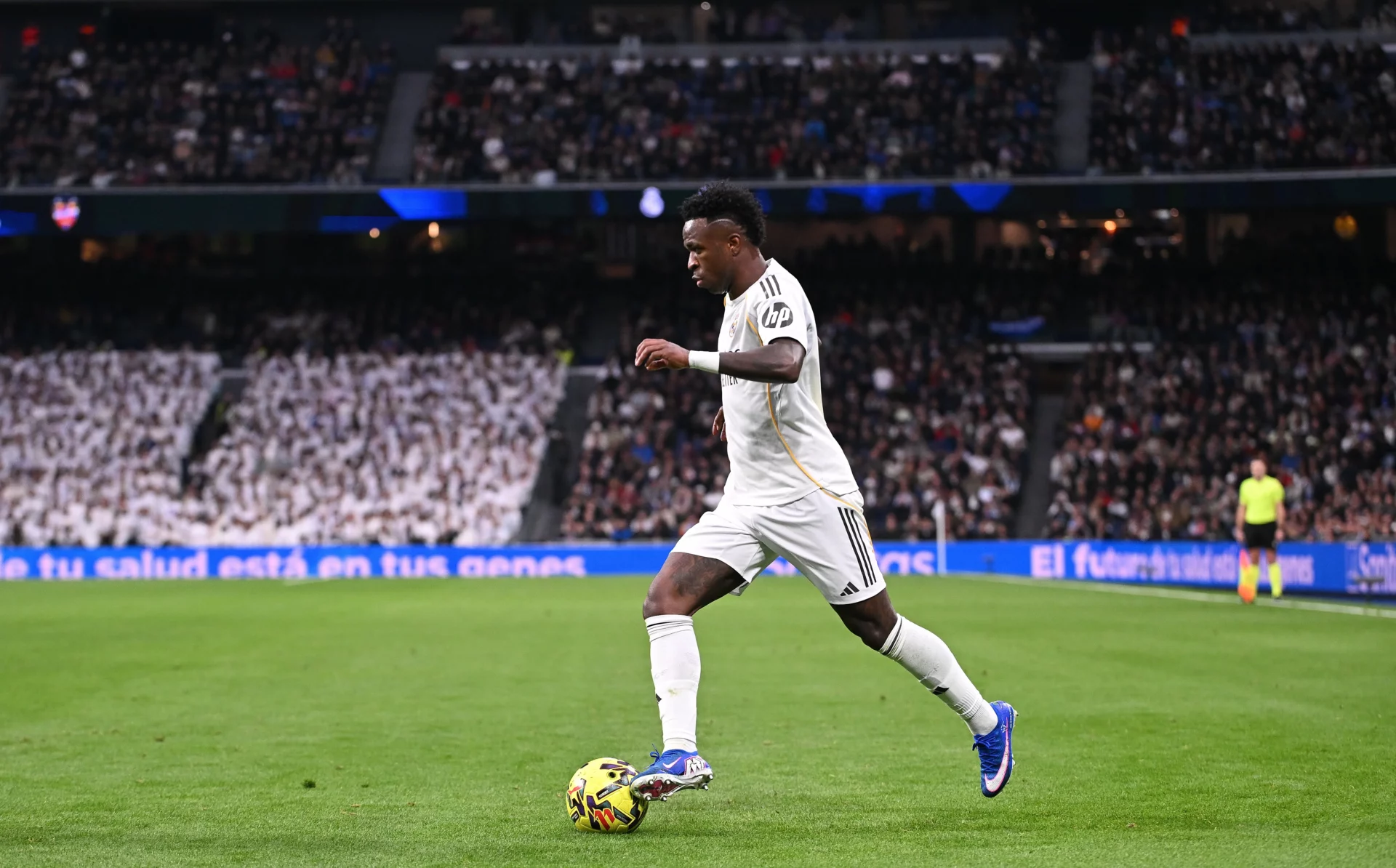 Vinicius conduce el balón durante un partido del Real Madrid con el público de fondo en el Bernabéu.