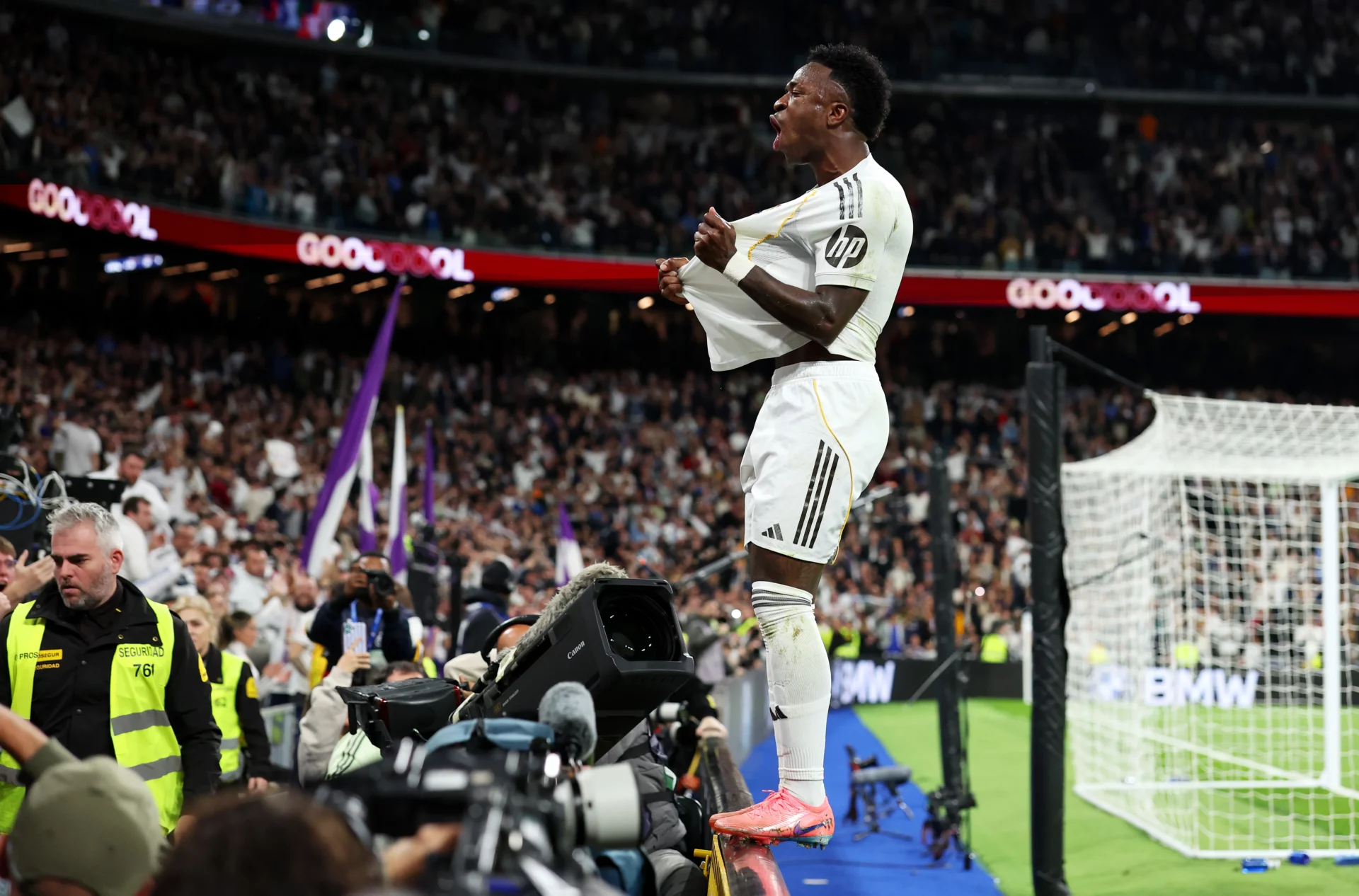 Vinicius celebra, subido a la valla de publicidad, con la grada uno de sus goles al Atlético.