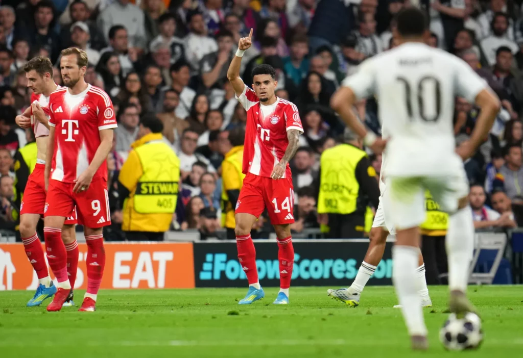 Luis Diaz celebra su gol contra el Real Madrid en la Champions League, con Kylian Mbappé esperando para sacar de centro.